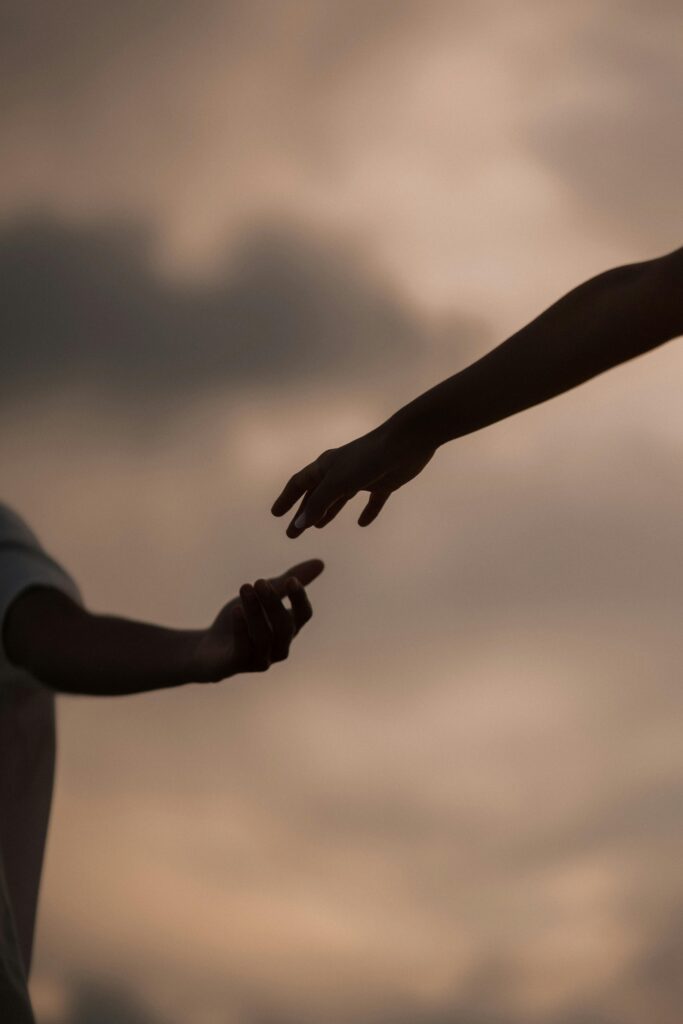 Silhouette of two hands reaching towards each other at sunset, symbolizing connection and hope.